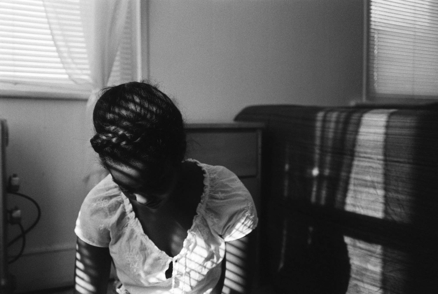 Jonelle photographed in her bedroom as shadows from the blinds fall on her face. Made with a Leica M2 on Ilford HP5+.