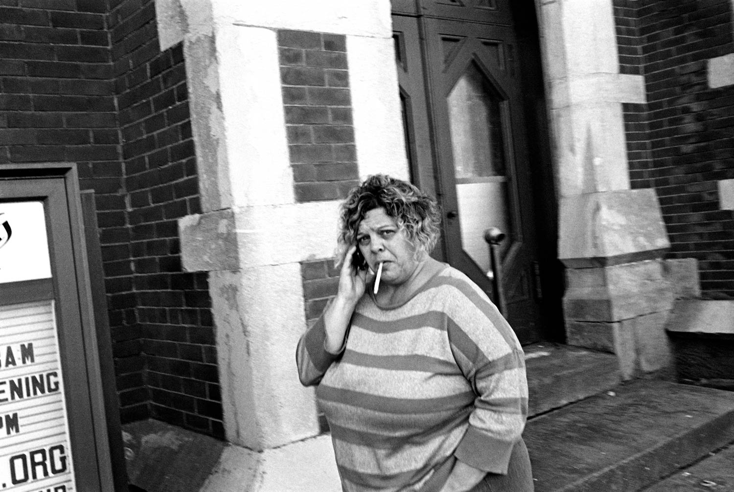 A black and white street photography of a woman talking on her cell phone and smoking on the streets of Binghamton, NY.