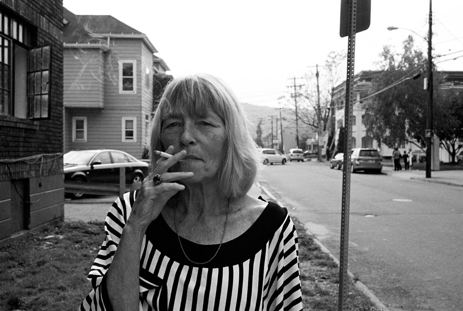 Black and white street photograph of an older woman in a vertical stripe shirt smoking a cigarette in Binghamton, NY.