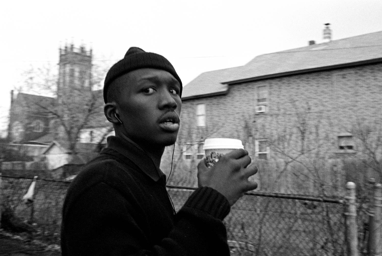 Close-up black and white street photography of a man looking at the camera with a surprised expression with a coffee cup in his hands. Taken with a Leica M2 and Ilford HP5+.