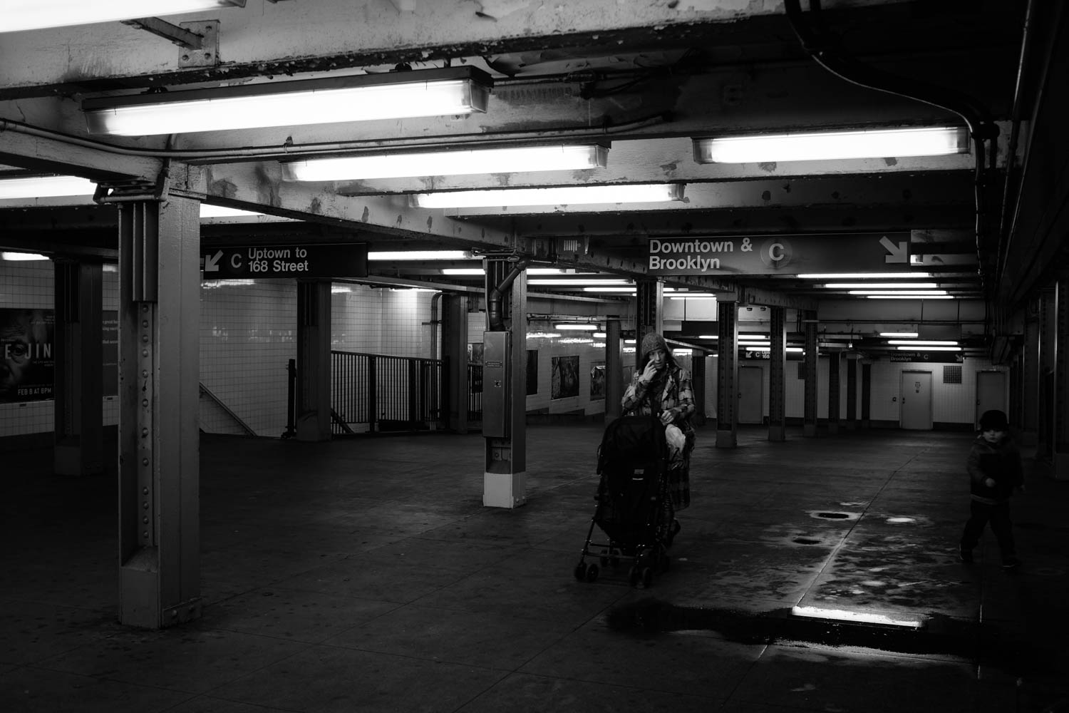 A black and white photograph of a woman pushing a stroller through a New York City subway station.