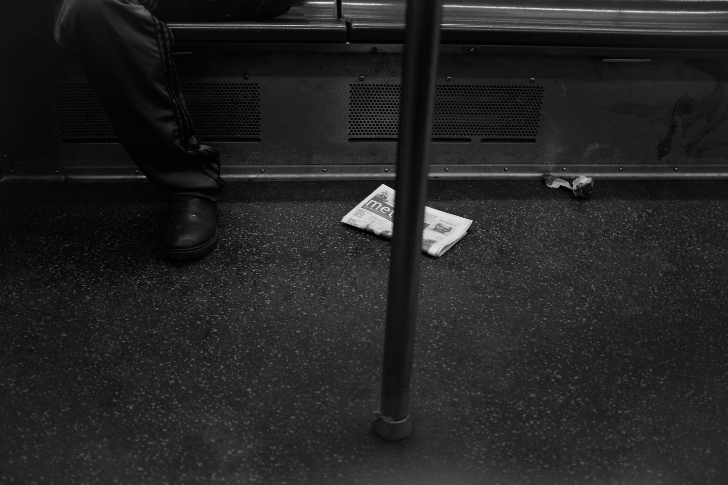 A black and white photograph of a newspaper on the floor of a subway car.