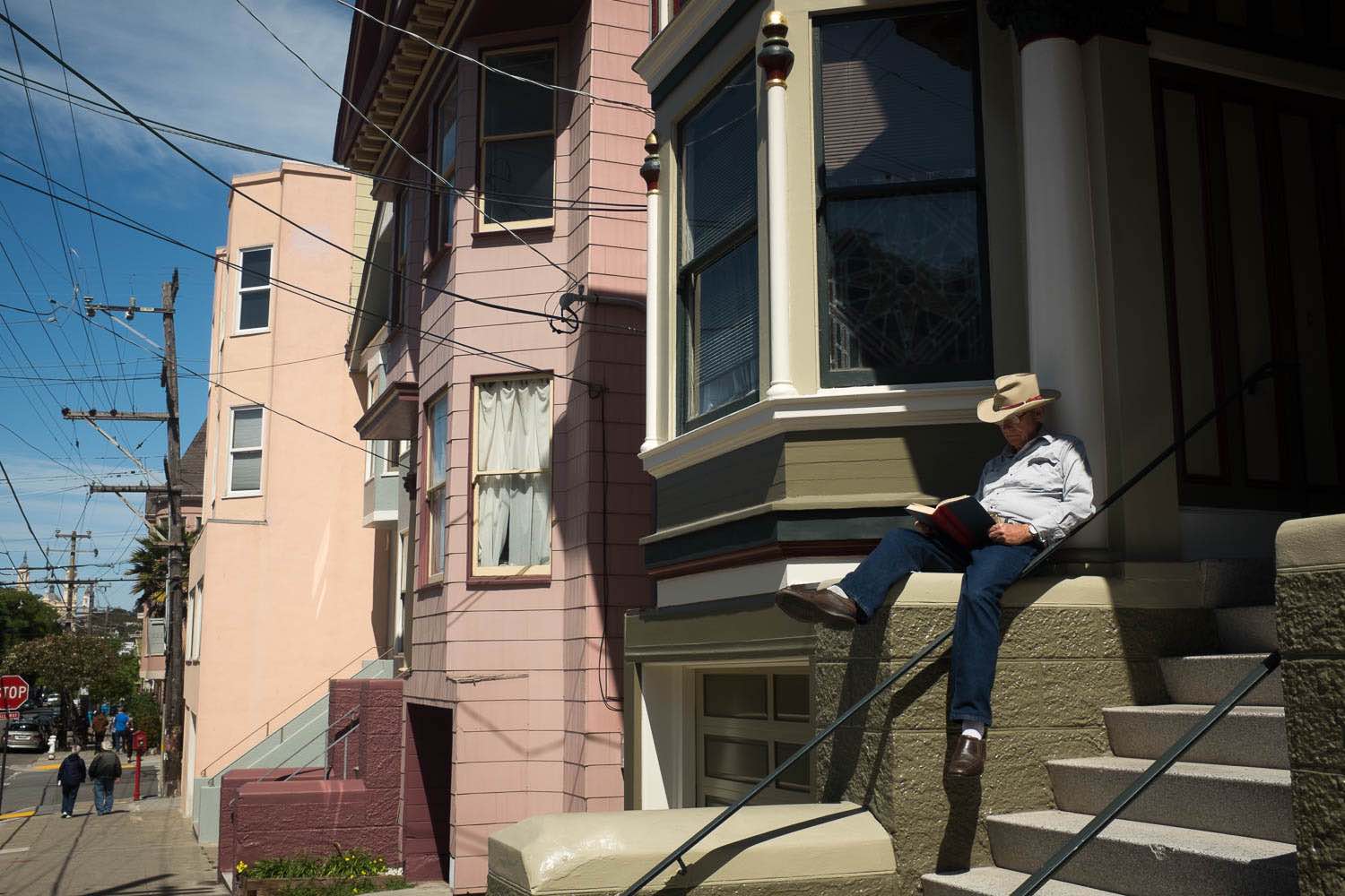 A man in a cowboy hat reading a book on his front steps in San Francisco